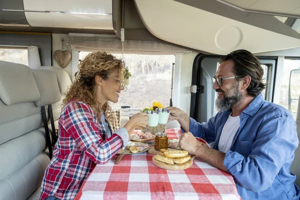 Travel on camper van lifestyle. Alternative vehicle vacation living van life off grid. People having lunch. Man and woman couple toasting with plastic glass and enjoying indoor leisure on motor home car