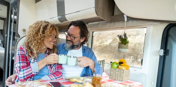 Adult couple toasting inside camper van during travel adventure life vacation. Motor home camper vehicle indoor leisure activity. Concept of traveler and people living offgrid in van life style.