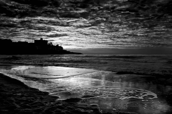Dramatic black and white sea landscape image with dark sky and white waves. City in background. Fine art seascape.