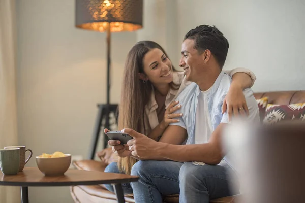 Couple in love resting on comfy couch having fun using smartphone apps, enjoy distant video call, boy showing interesting website to girlfriend, choosing services goods on-line e-commerce concept