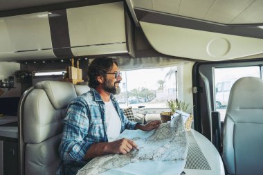 Happy mature man smiling inside a camper camping car using paper map guide to plan destinations holiday. Van life lifestyle alternative people. Living off grid and travel. Van life modern people