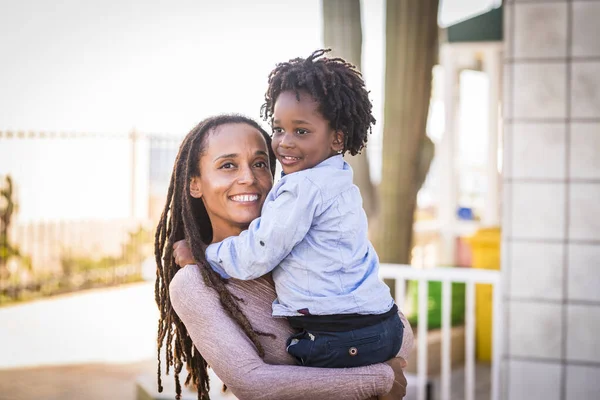 happy black ethnic family Afro-American mother and son hug together outside home in outdoor leisure activity. Mommy and little boy having fun with love and friendship