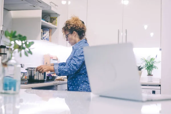 女人在家独自做饭 用罐子和笔记本电脑看网上新菜谱 在白色厨房里 准备食物是真正的休闲活动 现代女士白天做饭 — 图库照片