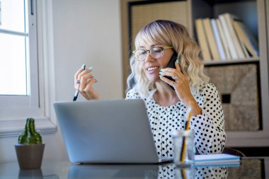 Cheerful woman freelance in smart working busy office home activity alone sitting at the desk and phone call. Concept of online modern alternative job. Businesswoman smiling and speaking on cell