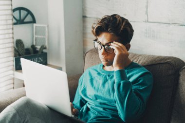  Genç bir çocuk evde tek başına bilgisayar kullanıyor ve gözlük takıyor. Sıkıcı ve yorgun adam evde bilgisayarla çalışıyor. Modern internet bağlantısı olan alternatif okul dersleri kavramı