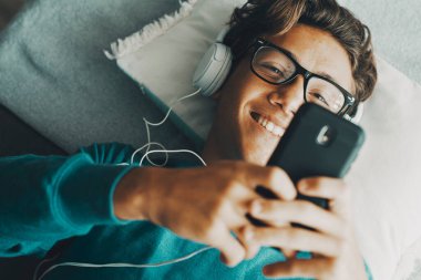 Neşeli genç çocuk kulaklıkla müzik dinlemek için telefon kullanıyor. Modern insanlar internette cep telefonu cihazıyla sohbet edip flört ediyorlar. İnternette sörf yapmaktan hoşlanan öğrencilerin boş vakitleri
