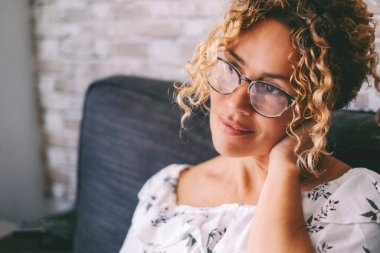 Huzurlu yüz ifadesi olan kadın evde tek başına gülümseyip boynuna dokunuyor ve gözlük takıyor. Ön tarafa bakan orta yaşlı kadın portresi. Sağlıklı ve sağlıklı bir yaşam tarzı olan insanlar rahatlar.