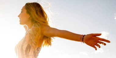 Başarı ve mutluluk ya da özgürlük düşünceli konsept yaşam tarzı. Güneşe doğru uzanan kollarını açan güzel bir kızın yan görüntüsü. Sağlıklı ve keyifli açık hava eğlence aktivitesi. Seyahat