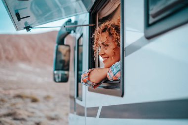 Bir kadın turist, pencereden dışarı bakan bir karavan aracının içinde özgürlüğün ve manzaranın tadını çıkarıyor. Göçebe yaşam ve Vanlife bağımsız modern insanlar kavramı. Yeni bir ev tarzı. Aktarım