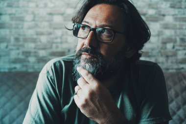 Çenesine dokunan düşünceli bir adamın portresini yakından çek ve gözlükleriyle kanepeye bak. Yetişkin ve yalnız bir adam çözüm düşünüyor. Olgun insanlar ve aile ekonomisi düşünceleri zorluyor