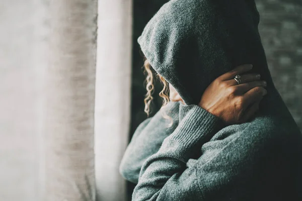 Desperate woman at home indoor wearing sweater with hood on and touching her neck. Stress and life problems for female people alone. Loneliness and depression medical concept. Housewife sad and lonely