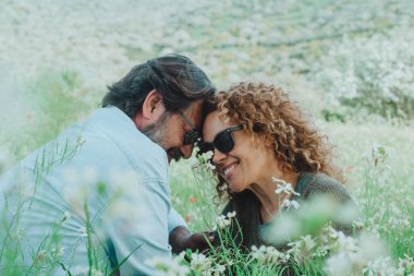 İlişki yaşam tarzında aşk ve romantizm. Çiftler randevudan ve hayattan keyif alıyorlar. Yeşil doğa tarlasında beyaz çiçeklerle oturuyorlar. Mutlu erkek ve kadın açık havada eğleniyor