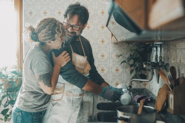  Adam, ev işlerinde karısına yardım ediyor mutfakta bulaşıkları yıkıyor. Kadınlar, ev işlerinde, boş zamanlarında kocasına yardım etmeyi sever. Çift gülüyor ve sevgi ile sarılıyor.