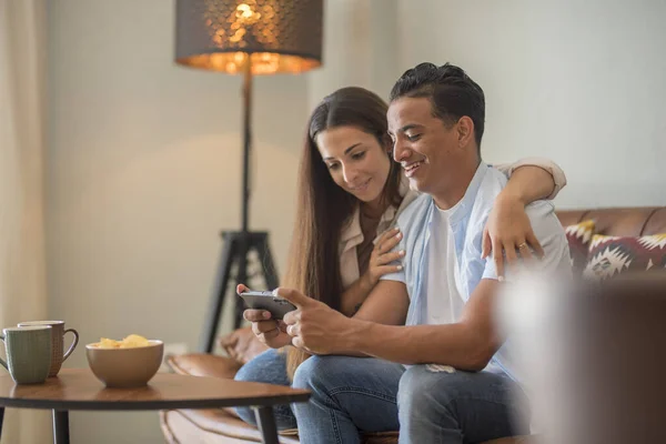 现代男女青年夫妇使用手机放松地坐在沙发上笑着 玩得很开心 黑人男孩和白人女孩喜欢用手机上网和社交媒体 — 图库照片
