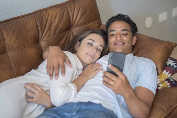 在室内休闲活动中 年轻夫妇一起用手机躺在沙发上放松一下 恋爱和恋爱中的黑人男孩和高加索女孩 亲密的人享受着 — 图库照片