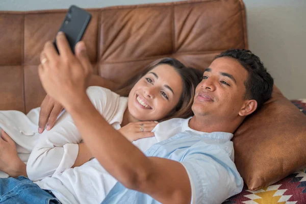 约会和关系 年轻夫妇 跨种族的黑人男孩和高加索女孩在室内休闲活动中享受时光 他们用手机把自己的照片放在沙发上 — 图库照片