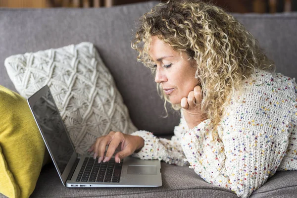 疲惫的女人躺在家里的沙发上 用笔记本电脑上网 让人厌烦的表情 沉迷于社交媒体 抑郁症 孤独的成年女性独自在室内笔记本电脑上写作 — 图库照片