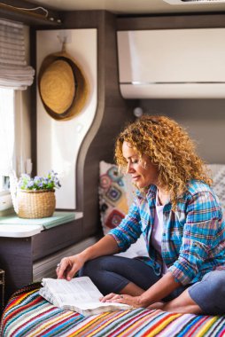Rahat, yetişkin bir kadın, karavan yatak odasında, yatakta rahat bir şekilde oturup kitap okumaktan zevk alıyor. Seyahat ve mutluluk. Küçük ev karavanı.
