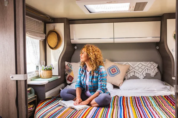 One woman having relax indoor leisure activity in tiny house camper van bedroom sitting on bed and looking outside the window. Happiness and serene people concept lifestyle. Healthy and travel concept