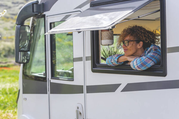 Serene tourist adult woman enjoy peaceful destination travel looking outside the window of camper van rv vehicle motor home and smiling. Vehicle transport and vacation lifestyle people. Dreaming happy