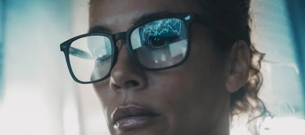 Close up of woman face with charts reflecting on eyewear. Female modern digital worker watching computer display. Serious lady expression portrait. Blue light mood. Futuristic. Crypto exchange job