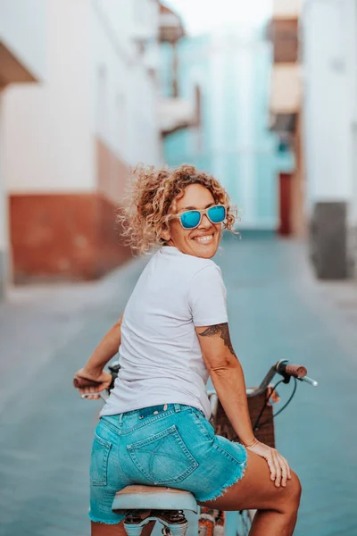 Cheerful active woman riding a bike in the street town and looking back smiling. Green transport and active healthy lifestyle people. Female enjoying bicycle in city transportation concept lifestyle