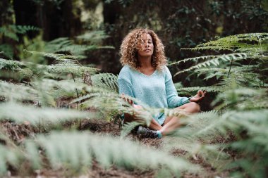 Health natural lifestyle meditation woman in the forest park with green tropical leaves all around.  healthy female people in yoga lotus position sitting on the ground in the woods. Wellbeing clipart