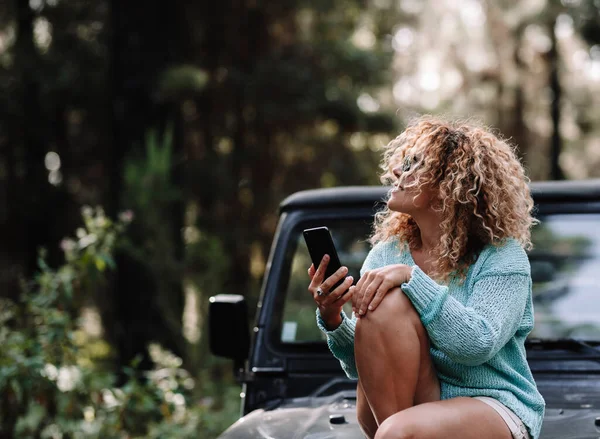 女旅行者坐在前车上 使用手机连接技术 享受户外车辆休闲活动的乐趣 妇女与自然 森林和交通概念 — 图库照片