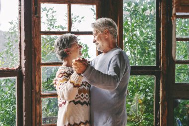 Mutlu son sınıf çifti evde romantik bir şekilde dans ederek ve sonsuza dek birlikte olmanın tadını çıkararak kutluyor. Yaşlı adam ve kadın ahşap dağ evinde samimi dans ediyorlar.