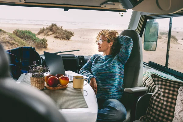 Living and working inside camper van vehicle in travel and digital nomad free lifestyle.  woman sitting in a motor home and enjoy relax and laptop connection. Beach in background outside the window