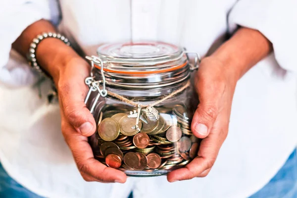 Woman hands holding a glass jar full of coins saving to travel and realize dreams lifestyle. People and money budget concept. Wanderlust adventure. Europe and euro economy crisis