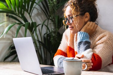 Mutlu kadın portresi ev içi rahatlama aktivitesi dizüstü bilgisayarın önünde görüntüleme ve çevrimiçi içerik. Modern kadın gözlük takıyor ve masada tek başına bilgisayar kullanıyor.