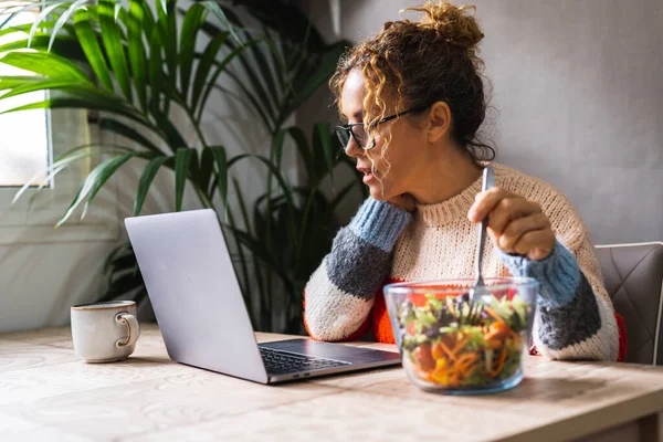 昼休みにはパソコンの前で速く健康的な食事をする人もいます 家庭で働く現代のビジネスライフスタイル 一人の女性がテーブルの上の透明なボウルからサラダを食べる — ストック写真