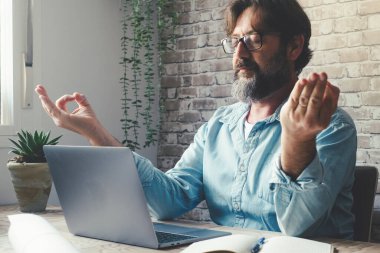 Bilgisayarda işten sonra dinlenen olgun bir adam. Ev ofis konseptinde aşırı çalışma ve sağlıklı rahatlama egzersizi akıllı çalışma tarzı. İnsanlar ve internet işi. Yoga yapan biri.