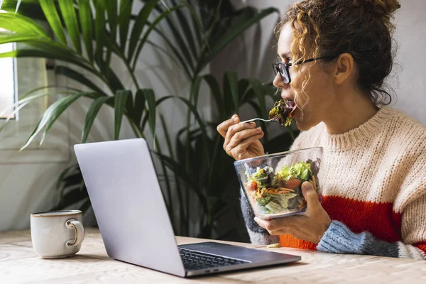 现代女商人在家庭工作中的形象 室内休闲活动 吃沙拉 在电脑上工作 午休时间和业务繁忙的人 饮食健康的女性吃蔬菜 — 图库照片