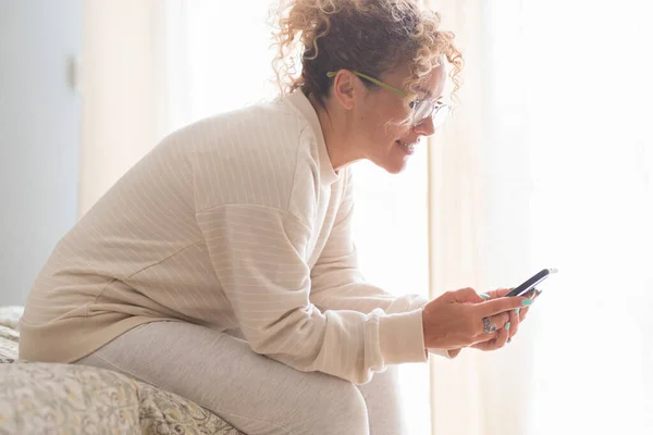 Vista Lateral Mujer Adulta Usando Teléfono Casa Sonriendo Sentado Cama —  Fotos de Stock