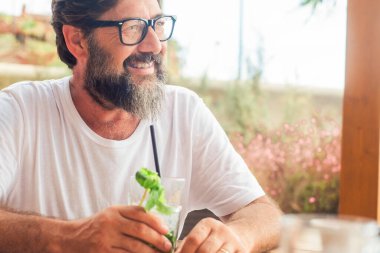 Tatil tatili için açık hava aktivitelerinde kafeterya barında mojito içen mutlu yetişkin bir adamın portresi. Turistler dinleniyor. Masada oturmuş gülümseyen olgun bir erkek.