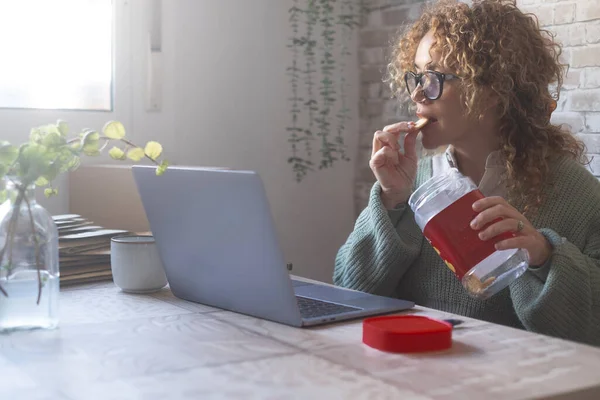 家で一人でウェブをサーフィンしてる女性箱からクッキーを食べながらオンラインコンテンツを見てる 人々と食中毒 自宅で現代的なライフスタイル オフィスの中年労働者の肖像 — ストック写真