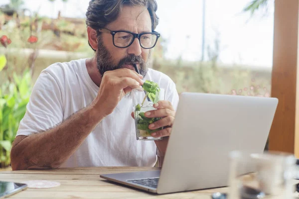 ノートパソコンの画面で読書をしたり バーで新鮮な夏のカクテルを飲んだりするビジネスマン ワイヤレスシェア接続のカフェで働く人 — ストック写真