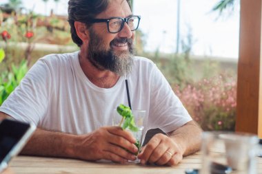 Tatil tatili için açık hava aktivitelerinde kafeterya barında mojito içen mutlu yetişkin bir adamın portresi. Turistler dinleniyor. Masada oturmuş gülümseyen olgun bir erkek.