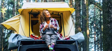 Arabasında çatı çadırı olan özgürlük ve alternatif kamp çözümleri. Bir maceraperest kadın orman ormanlarında çadırının dışında yalnız başına alternatif tatilin tadını çıkarıyor. Özgürlük ve yolculuk yaşam tarzı