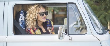 Klasik mavi minibüsündeki turist görüntüsü gülümsüyor ve seyahat yaşam tarzının tadını çıkarıyor. İnsanlar ve ulaşım konsepti. Minibüsün içinde modaya uygun bir bayan var. Gülümseyin.