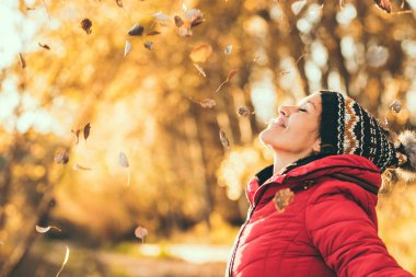 Mutluluğun ve özgürlüğün ifadesi. Neşeli kadın sonbahar renklerini ve parktaki boş vakitleri örgü şapka ve kırmızı ceket giyerek geçirmeyi seviyor. Mutlu insanlar yan görünüm portresi. Sarı
