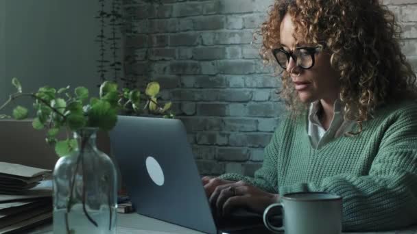 女人坐在办公室的桌子旁 在昏暗的夜色中 在笔记本电脑上写字 自由职业和现代聪明的人在计算机上工作的概念 自由生活的夜晚 — 图库视频影像