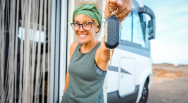 Minibüs karavanı fuarının yeni alıcısı, kameranın karşısında anahtarlarını mutlulukla gösteriyor. Tatil konsepti sahnesi için yeni ev ve araç. Vanlife tarzı seyahat et. Macera. Göçebe insanlar dişi