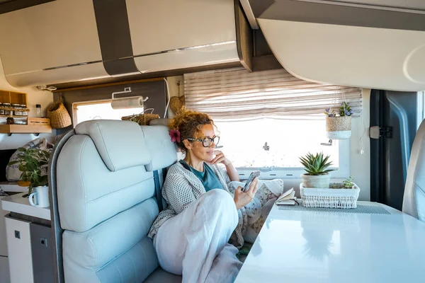 Adult woman relaxing inside a modern luxury camper van rv vehicle motorhome reading notification on cell phone. Alternative home vanlife style and tourism renting van. Tiny house. Traveler lifestyle