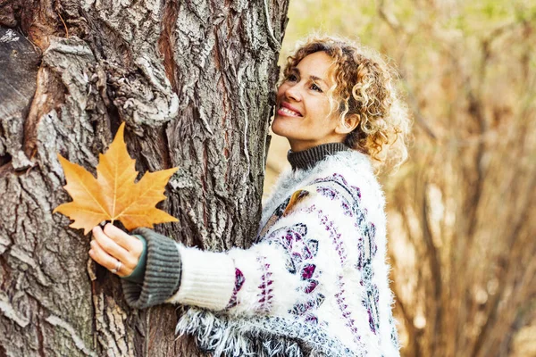 happy adult woman hug a tree and smile in autumn season outdoor leisure activity. Natural lifestyle and love nature concept people. Yellow color woods and trees in background. Female enjoying park