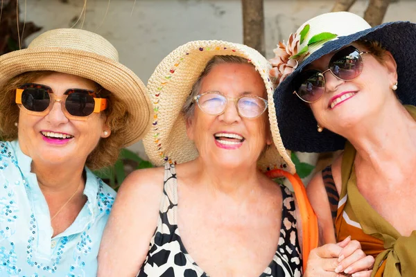 Outdoor portrait of three females old aged mature friends together having fun and smiling at the camera. Summer fashion lifestyle retired elderly people. Outdoor leisure activity together friendship
