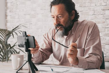 Ofisteki iş yerinde cep telefonunun önünde cep telefonuyla konuşan küçük bir işadamı. Evraklar masanın üstünde. Hücre iletişimiyle dijital çalışan profesyonel serbest