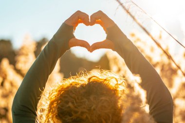 Turuncu ve sarı doğa parkı sahasında altın, güzel bir günbatımı ışığına karşı şömineyi yapan kadın ellerini kapayın. Mutlu ve özgür yaşam tarzı insanlar doğayı sever. Çevre ve sürdürülebilir konsept